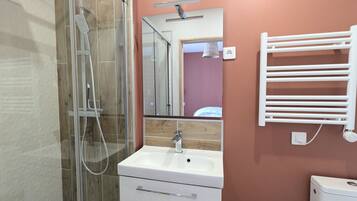 Een moderne badkamer met een douchecabine van glas, een witte wastafel en een spiegel erboven.