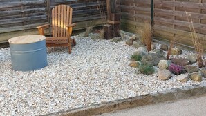 Une chaise en bois et un tonneau dans un jardin de gravier, avec une clôture en bois en arrière-plan.