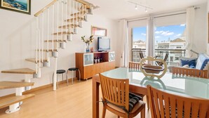 Een modern appartement met een houten trap, een eetruimte met een glazen tafel, en een balkon met uitzicht op gebouwen.