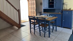 A dining area with a wooden table and chairs, a blue cabinet, and a staircase. - Vaux-sur-Mer: 2-Bed Villa for 5, 450m to Beach, Parking, AirCon (Vaux-sur-Mer)