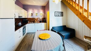 A modern kitchen with white cabinets, a wooden countertop, and a dining table with a patterned tablecloth. - Charming house 200m from beach for 5 people (Fouras)