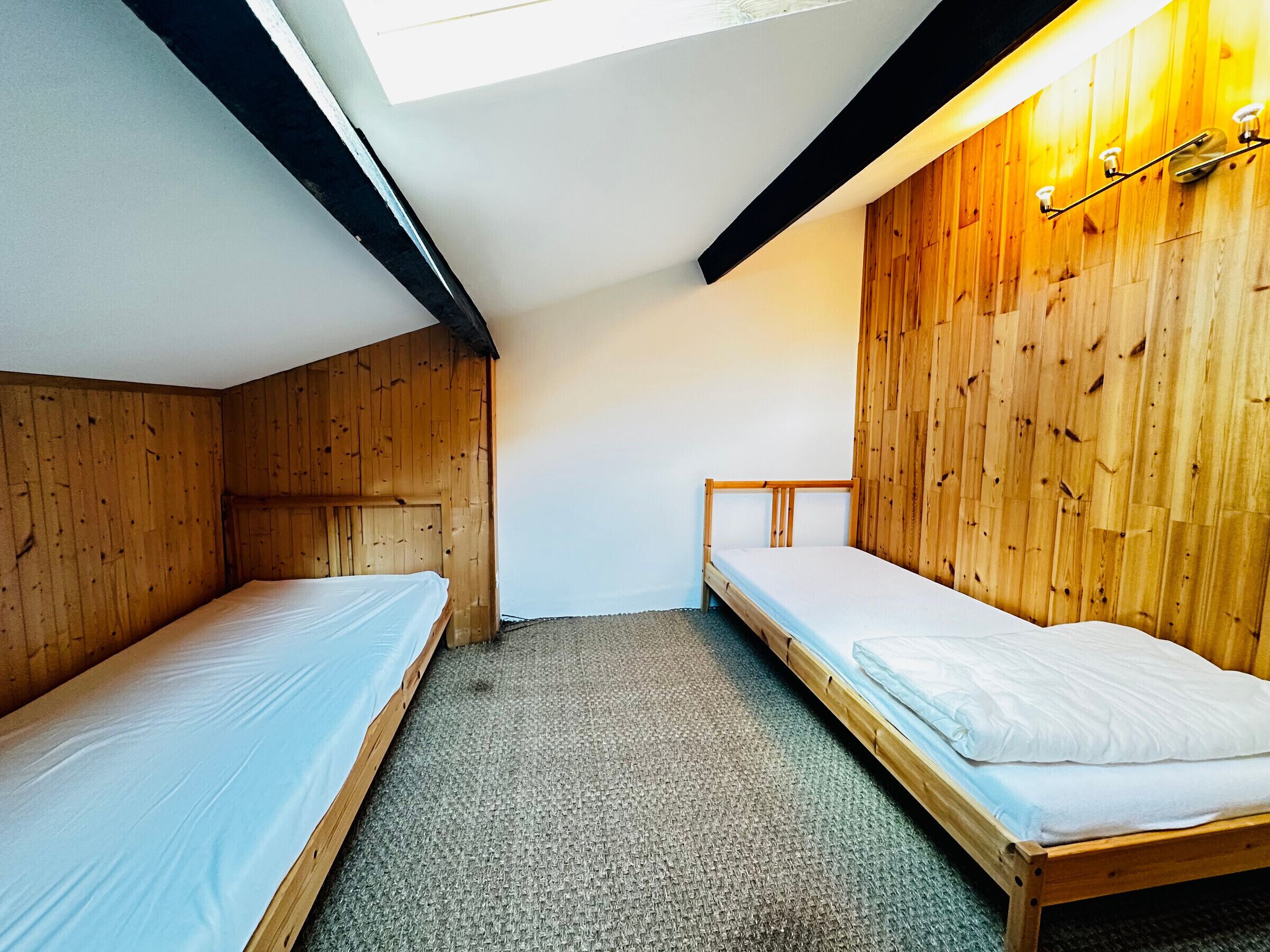 Un petit logement composé d’une seule pièce, avec deux lits superposés en bois, un plafond en pente et un puits de lumière.