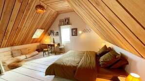 A cozy attic bedroom with a loft bed, a desk, and a chair.