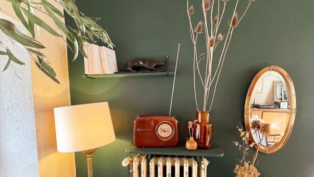 Una radio antigua, una lámpara, un radiador, un espejo y una estantería con libros y una figurita de gato.
