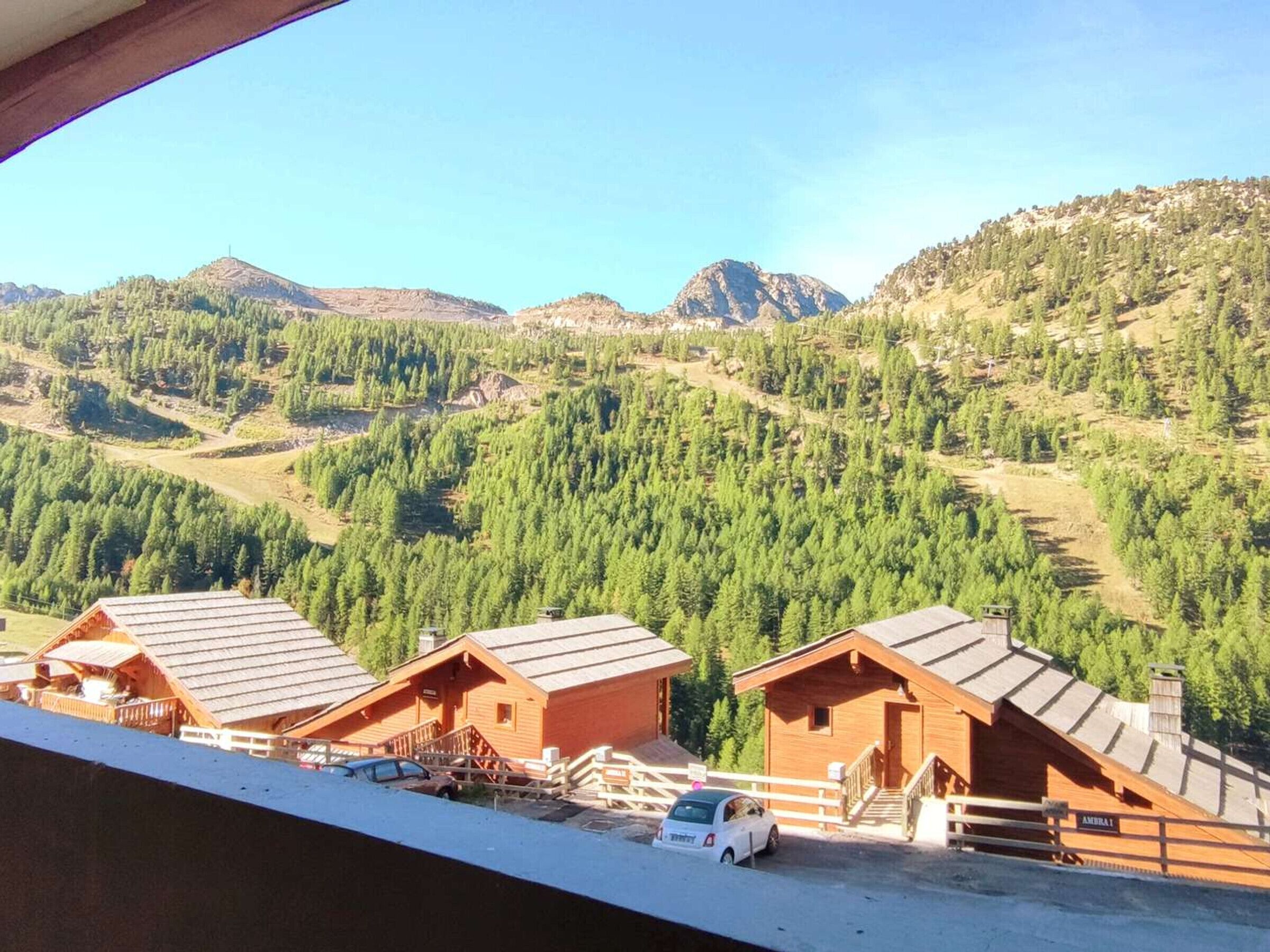 A mountain lodge with wooden cabins, a car parked in front, and a view of forested hills.