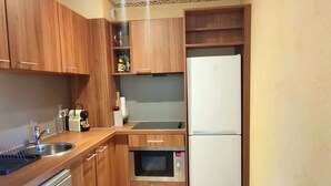 Une cuisine compacte avec des meubles en bois, un évier en acier inoxydable, un four encastré et un réfrigérateur blanc.