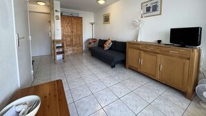 A living room with a sofa, TV, wooden cabinet, and a door leading to another room. - 2-room apt with parking, pool, sleeps 4, Cap d'Agde (Cap d'Agde)