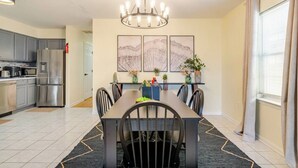A modern kitchen with stainless steel appliances, a dining area with a dark wooden table and chairs, and a chandelier. - 3BR Stay for Crews & Families (Elizabeth)