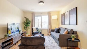 A modern living room with a sofa, armchairs, a coffee table, a TV, and a large window with curtains. - 3BR Stay for Crews & Families (Elizabeth)