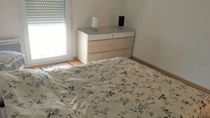 Ein Schlafzimmer mit floralem Bettbezug, einem Nachttisch mit Lampe und einem Fenster mit Jalousien.