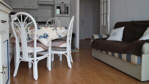 Ein kompakter Wohnbereich mit Essbereich, der einen Tisch, Stühle, eine Couch und eine kleine Küchenzeile im Hintergrund umfasst.