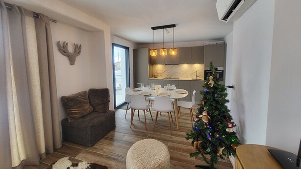 A modern living room with a sofa, a round ottoman, a Christmas tree, and a dining area with a table and chairs. - Montgenèvre Apartment with Terrace, Wifi & Parking (Montgenèvre)