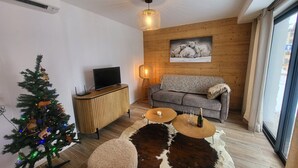 A modern living room with a wooden floor, a sofa, a coffee table, a TV on a wooden cabinet, a Christmas tree, and a polar bear painting on the wall. - Montgenèvre Apartment with Terrace, Wifi & Parking (Montgenèvre)