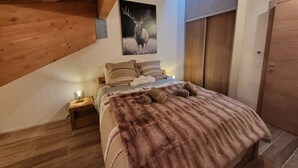Un dormitorio con techo de madera, una cama con un cubrecama de piel, una mesita de noche con una lámpara y una puerta con interruptor de luz.