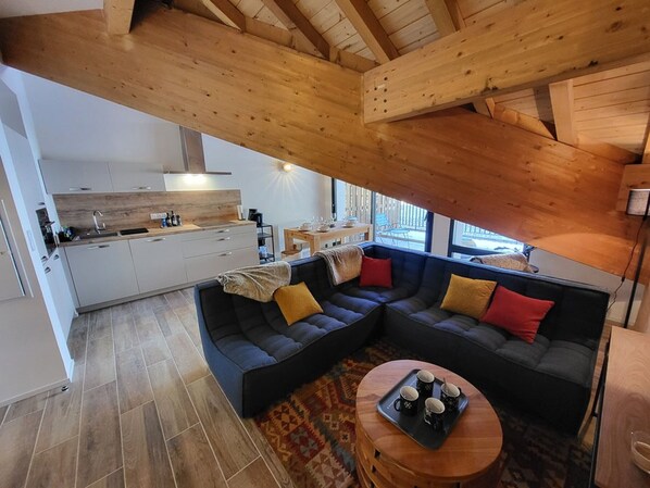 A modern kitchen with white cabinets and a wooden countertop, a dark-colored sofa with cushions, and a round wooden table with a tray of mugs. - Chamois Apartment with Wifi and Garage in Montgenèvre (Montgenèvre)