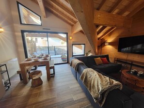 A cozy living room with a wooden ceiling, a sofa, a TV, and a dining area with a table and chairs. - Chamois Apartment with Wifi and Garage in Montgenèvre (Montgenèvre)