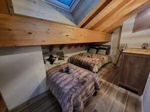 A loft-style bedroom with a sloped ceiling, wooden beams, and a skylight. There are two beds with plush bedding and a small bedside table with a lamp. - Chamois Apartment with Wifi and Garage in Montgenèvre (Montgenèvre)