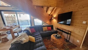 Una sala de estar acogedora con un sofá modular, un televisor de pantalla plana y un comedor con una mesa de madera y bancos.