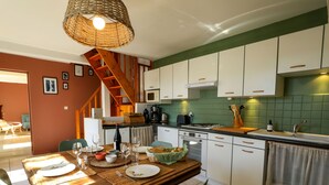 A modern kitchen with white cabinets, a wooden dining table, and a staircase leading to an upper level. - Family cottage between Angers and Saumur (Blaison-Saint-Sulpice)