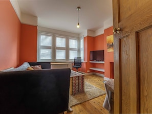 A living room with a sofa, a chair, a small table, a TV, and a wooden door.