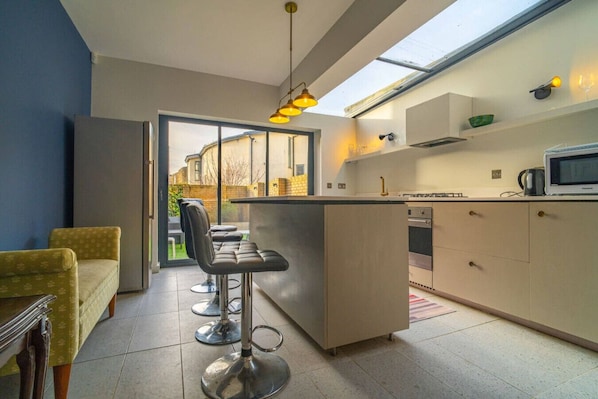 A modern kitchen with a bar area, a dining table with chairs, and a view through a glass door.