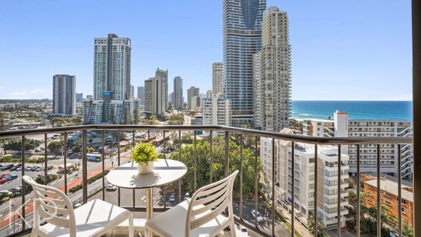 A balcony with a table and chairs, overlooking a cityscape with tall buildings and a beach.