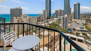 A balcony with a table and chairs overlooking a cityscape with high-rise buildings and a beach. - Ocean & City Views, Level 17, 5GInternet At Mantra (Surfers Paradise)