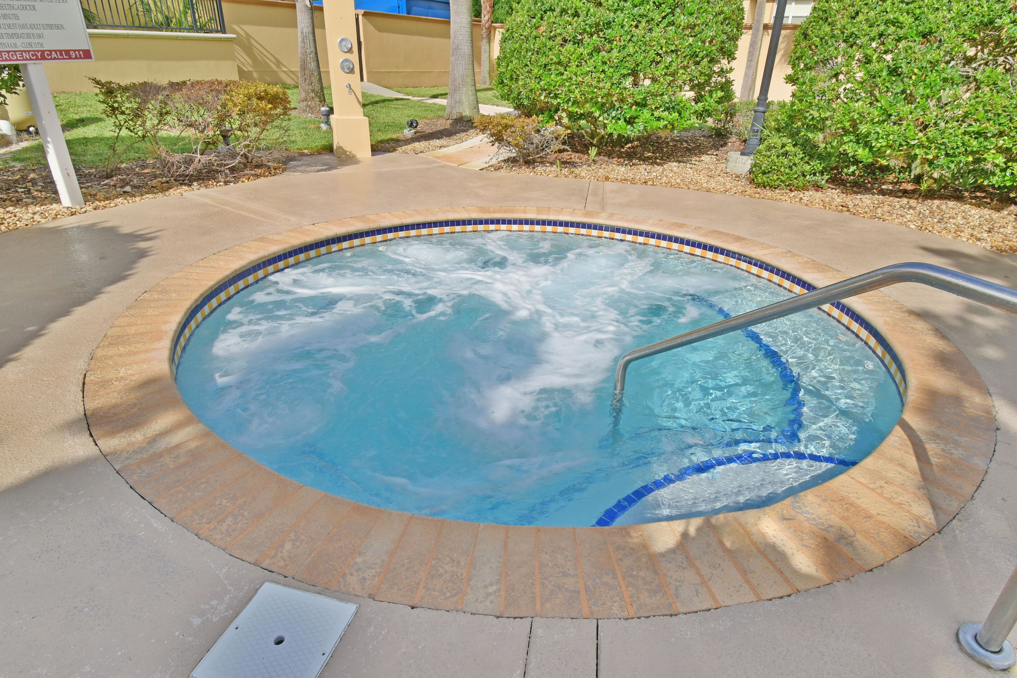 A hot tub with a metal ladder, surrounded by a tiled edge and a pebble border.