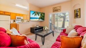 A living room with a red sofa, a glass coffee table, and a TV displaying a beach scene.