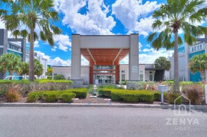 A modern building with a covered entrance, palm trees, and a clear sky. - Modern Condo in Reunion Resort Near Disney (Kissimmee)