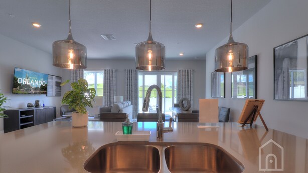 Une cuisine moderne dotée d’un grand îlot central, d’éviers en acier inoxydable et de luminaires suspendus.