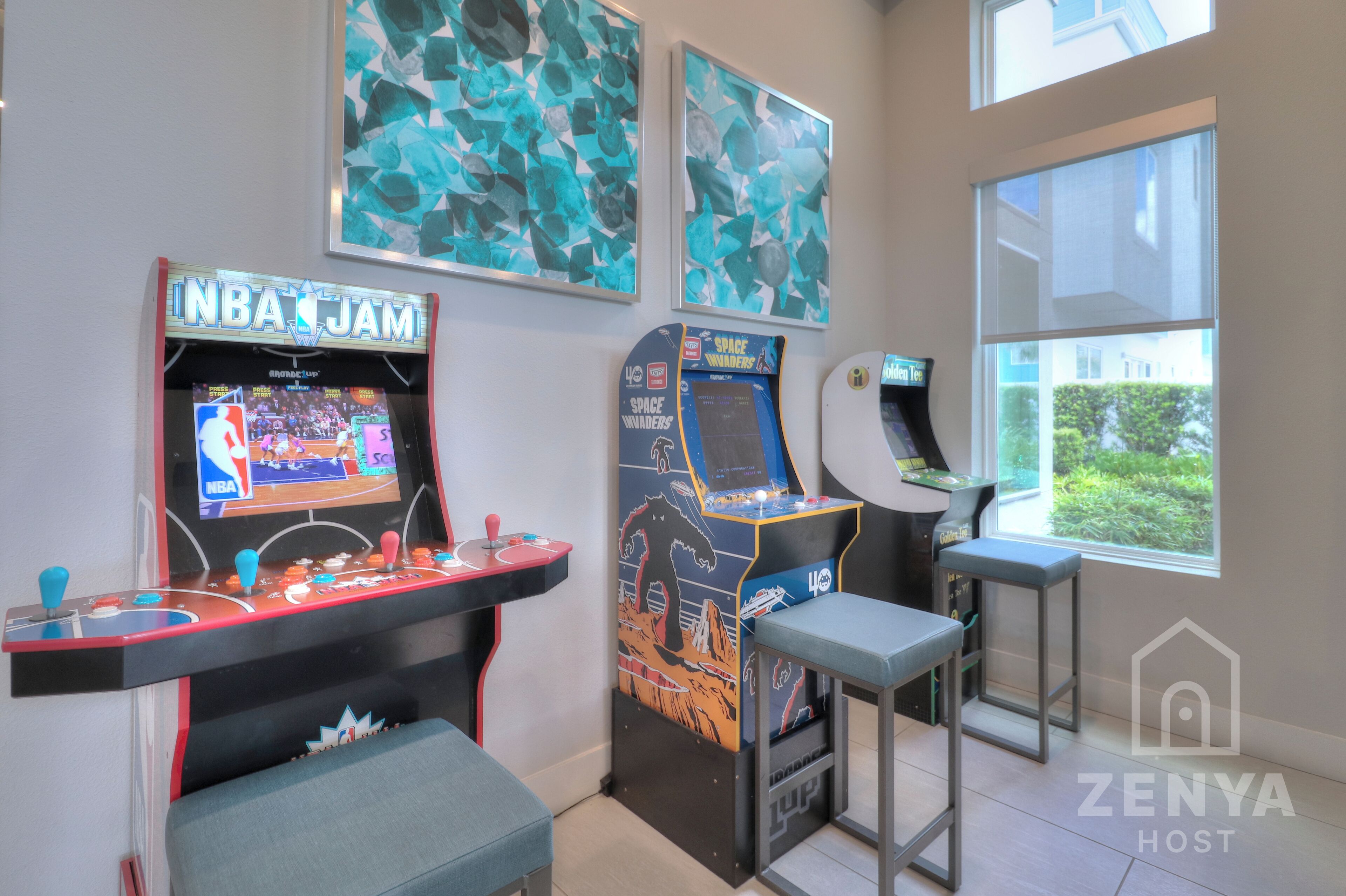 A gaming area with arcade machines, including NBA Jam and Space Warfighters, and a window with a view of greenery.