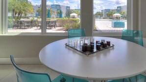 Une table ronde entourée de chaises, dans une pièce dotée de grandes fenêtres donnant sur une piscine et des bâtiments.