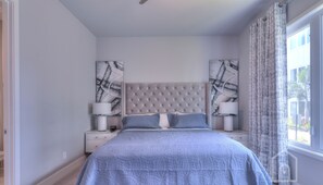 A bedroom with a tufted headboard, a large bed with a patterned bedspread, two bedside tables with lamps, and abstract artwork on the walls. - Modern Condo in Reunion Resort Near Disney (Kissimmee)
