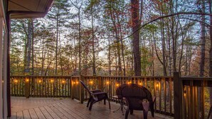 A wooden deck with chairs and string lights, surrounded by trees. - Play Arcade Games, Make Firepit S'mores & Explore Downtown Blue Ridge in Minutes - Trails End (Blue Ridge)