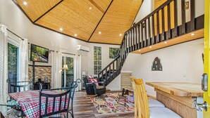 A spacious living area with a high ceiling, a wooden staircase, and a dining area with a checkered tablecloth. - Play Arcade Games, Make Firepit S'mores & Explore Downtown Blue Ridge in Minutes - Trails End (Blue Ridge)