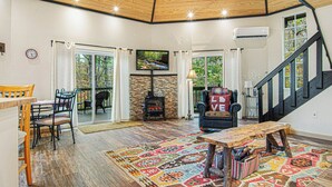 A cozy living room with a wooden ceiling, a fireplace, a comfortable armchair, and a dining area with a table and chairs. - Play Arcade Games, Make Firepit S'mores & Explore Downtown Blue Ridge in Minutes - Trails End (Blue Ridge)