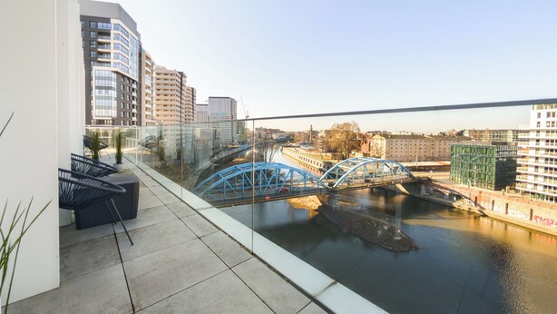 A balcony with a view of a river, a blue bridge, and modern buildings in the background. - Rynek Wrocław Luminous Apartment (Wroclaw)