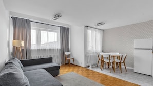 A modern living room with a grey sofa, a dining table with chairs, and a white refrigerator. - Mokotów Serene Apartment (Warszawa)