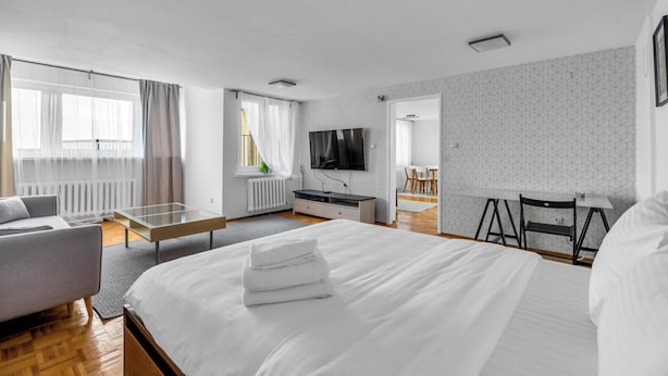 A modern hotel room with a large bed, a sofa, a desk, and a TV. - Mokotów Serene Apartment (Warszawa)