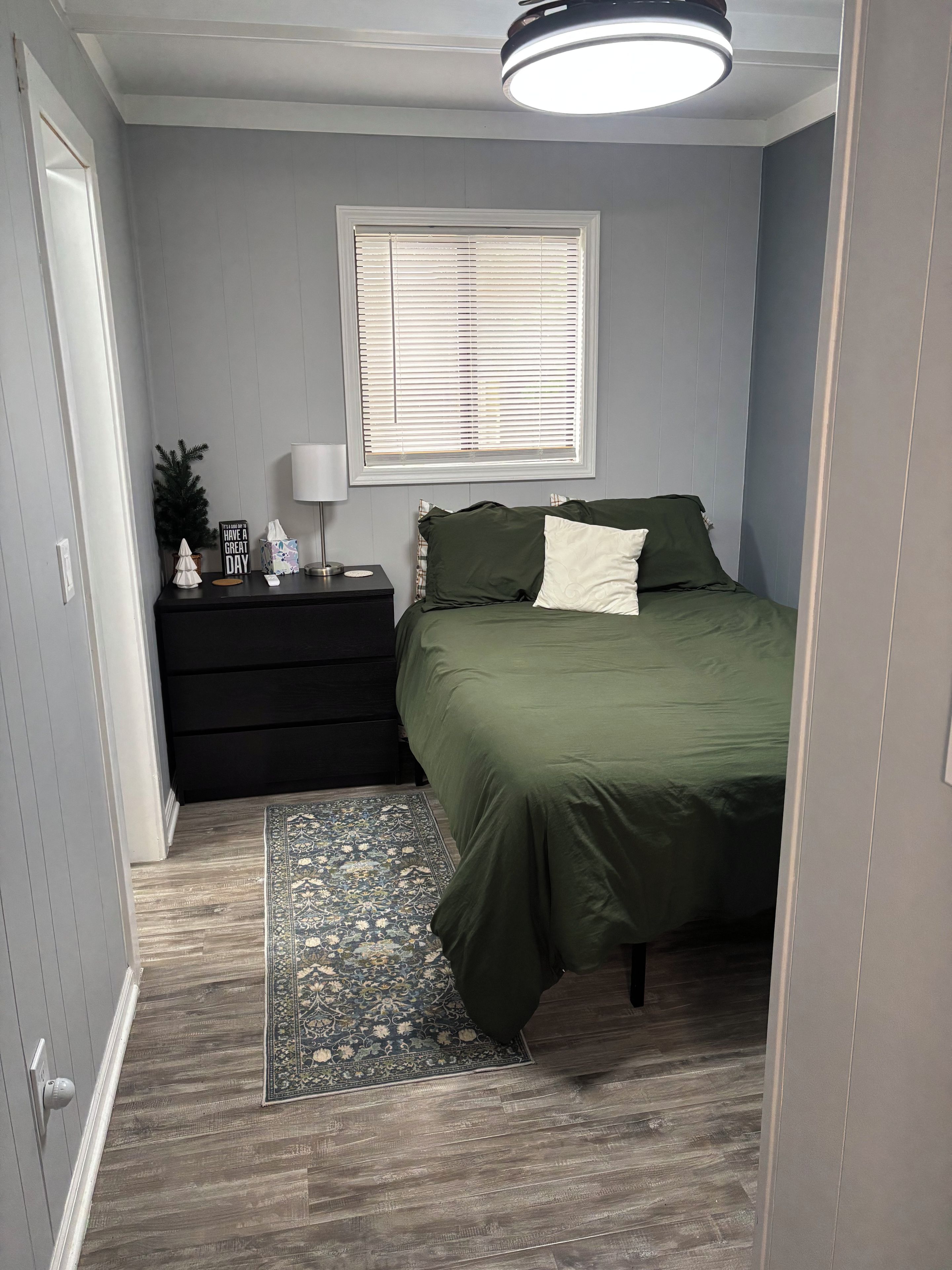 Une chambre à coucher avec un lit, une table de chevet, une lampe et une fenêtre avec des stores.