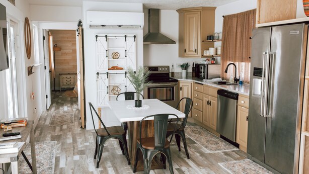 A modern kitchen with a central island, wooden cabinets, and stainless steel appliances. - The Chicken Coop (Nephi)