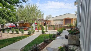 A residential area with a paved driveway, a wooden fence, and a variety of plants. - The Chicken Coop (Nephi)
