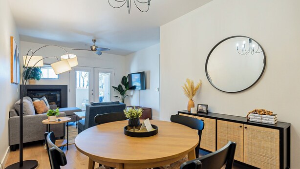 Ein modernes Wohnzimmer mit einem runden Holzesstisch, schwarzen Stühlen, einem grauen Sofa, einem Kamin und einem an der Wand befestigten Fernseher.