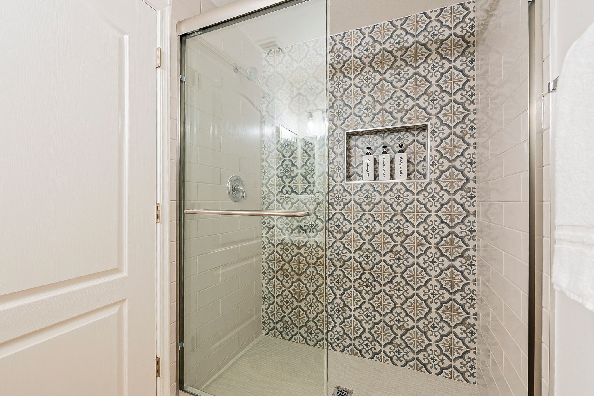 A shower with a glass door and patterned tiles.