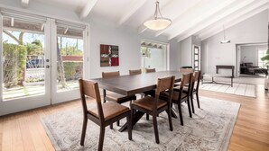 Un comedor amplio con una gran mesa de madera y sillas, una lámpara colgante y ventanas grandes que ofrecen vistas al exterior.