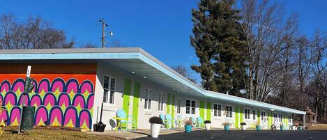 Un motel con paredes exteriores de colores vivos, varias habitaciones y mobiliario al aire libre.