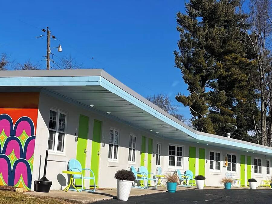 Un motel con paredes exteriores de colores vivos, varias habitaciones y mobiliario al aire libre.