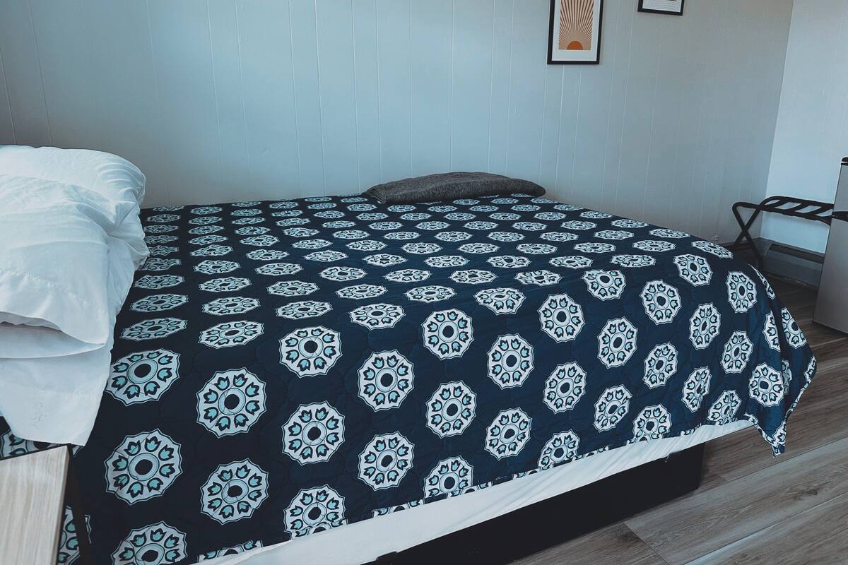 A neatly made bed with a patterned bedspread, a bedside table with a lamp, and a wall with two framed pictures.