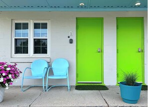 A building with two green doors, a window with blinds, and a blue chair outside. - The Springs Motel (Yellow Springs)